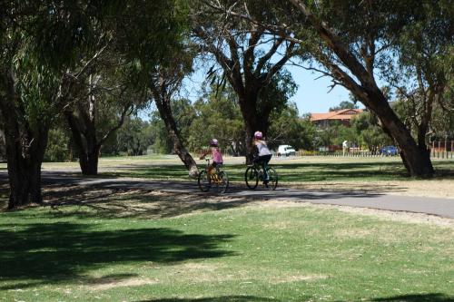 Two cyclist pedal on the sealed path through the open park land.