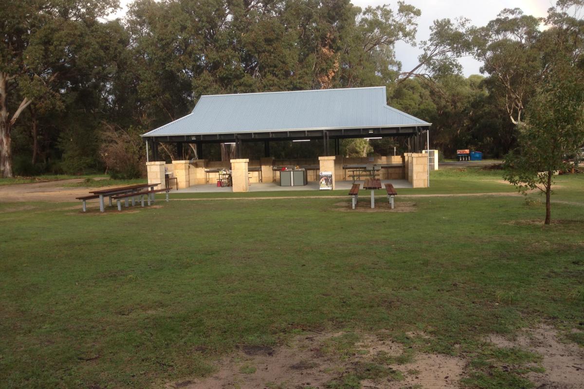 grassed area with long picnic tables and a camp cooking open air building