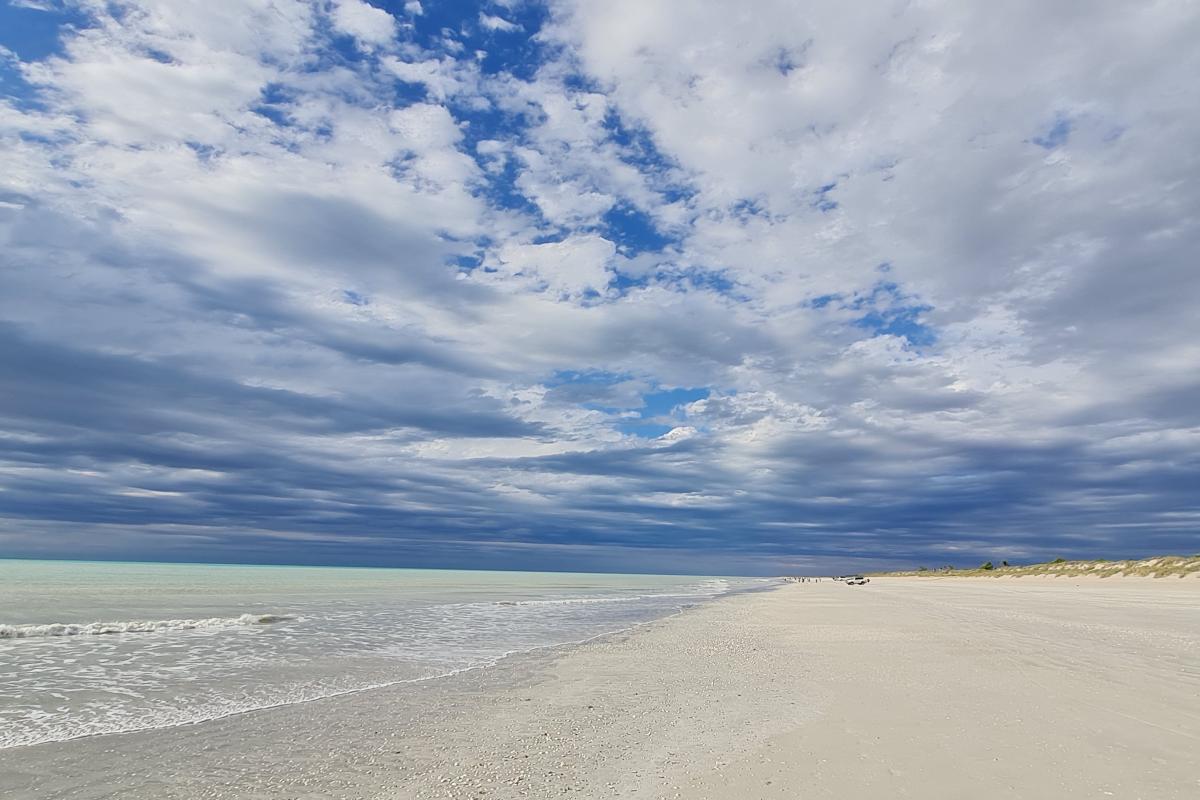 view of white sandy beach and blue water with blue cloudy skies