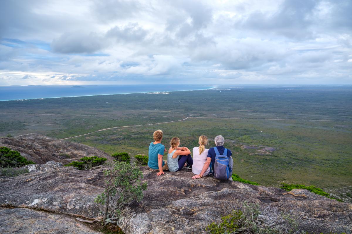 four people sitting on large rock with a view