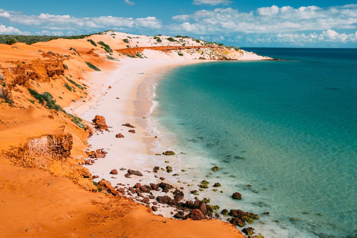 Colourful coastal bay of red dirt, white sand and calm green blue ocean.