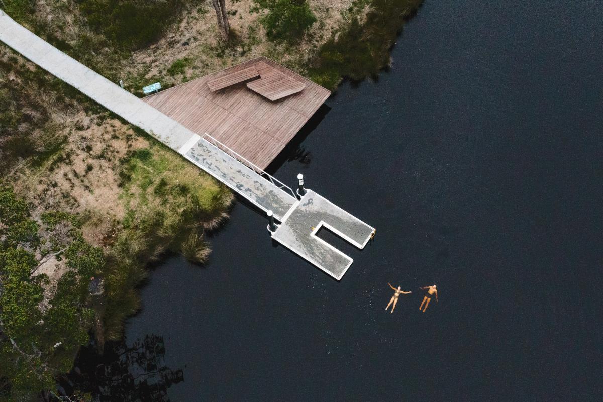 Aerial view of a jetty and two people floating in water. 